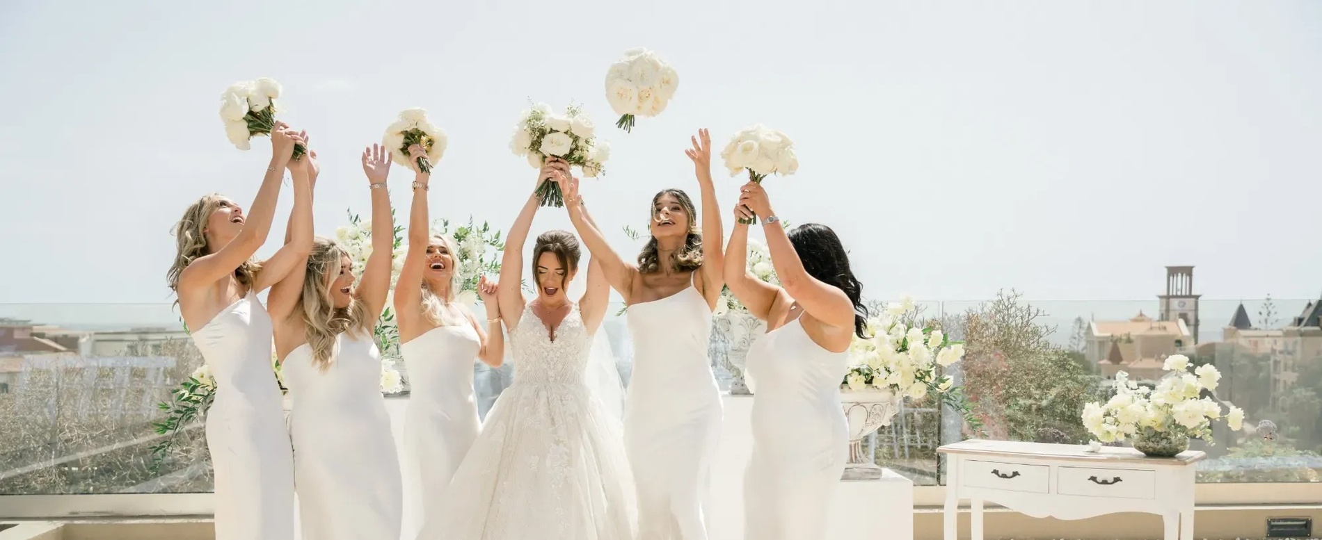 una novia y sus damas de honor sostienen sus ramos en el aire