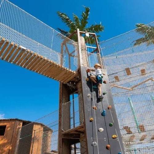un niño sube una pared de escalada junto a un puente de madera