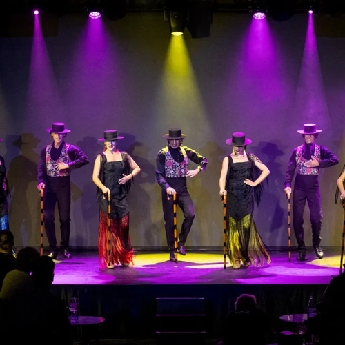un grupo de hombres y mujeres están bailando en un escenario con luces moradas y amarillas