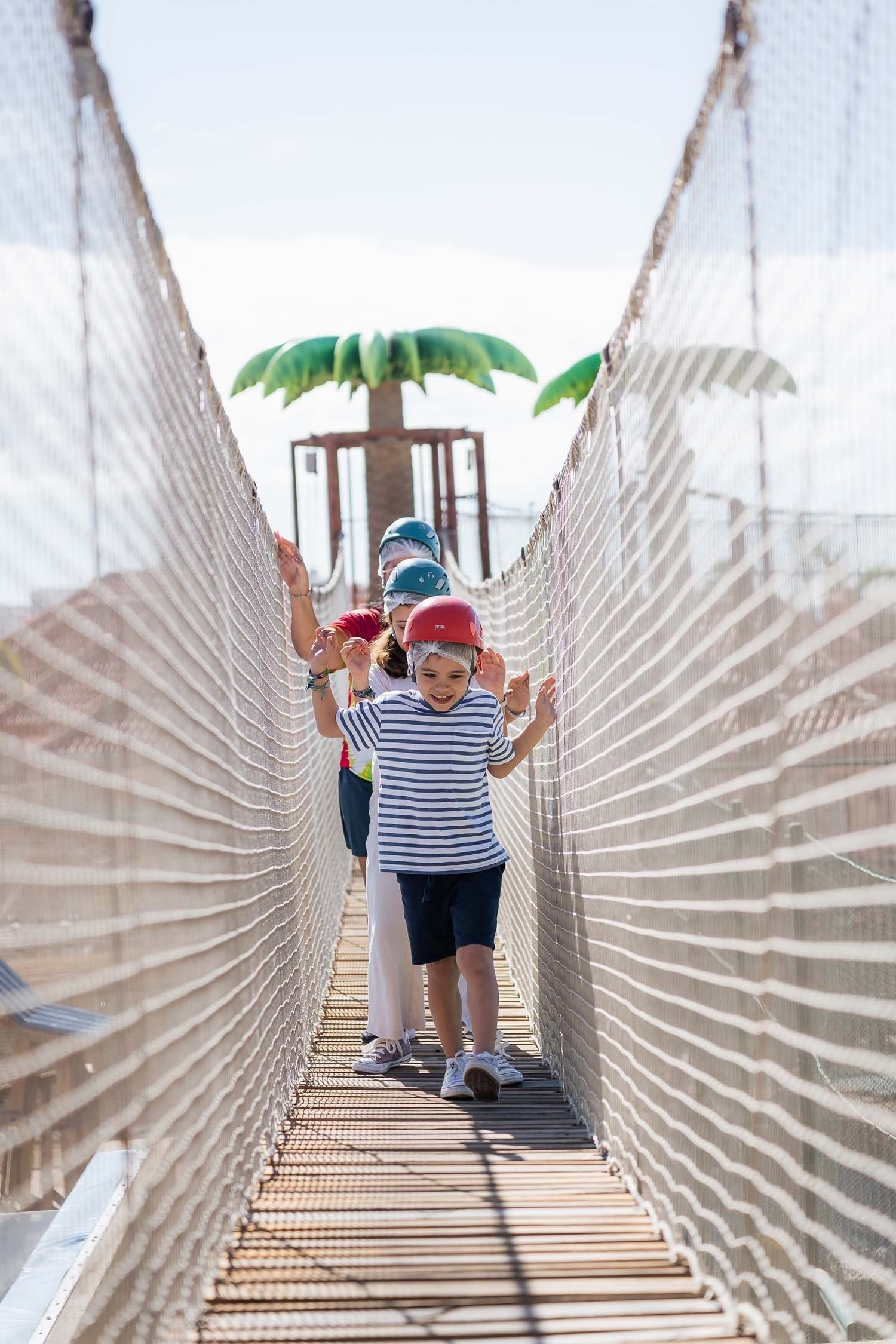 a group of children are walking across a rope bridge