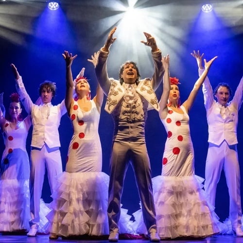 un grupo de hombres y mujeres en vestidos blancos con lunares rojos están actuando en un escenario