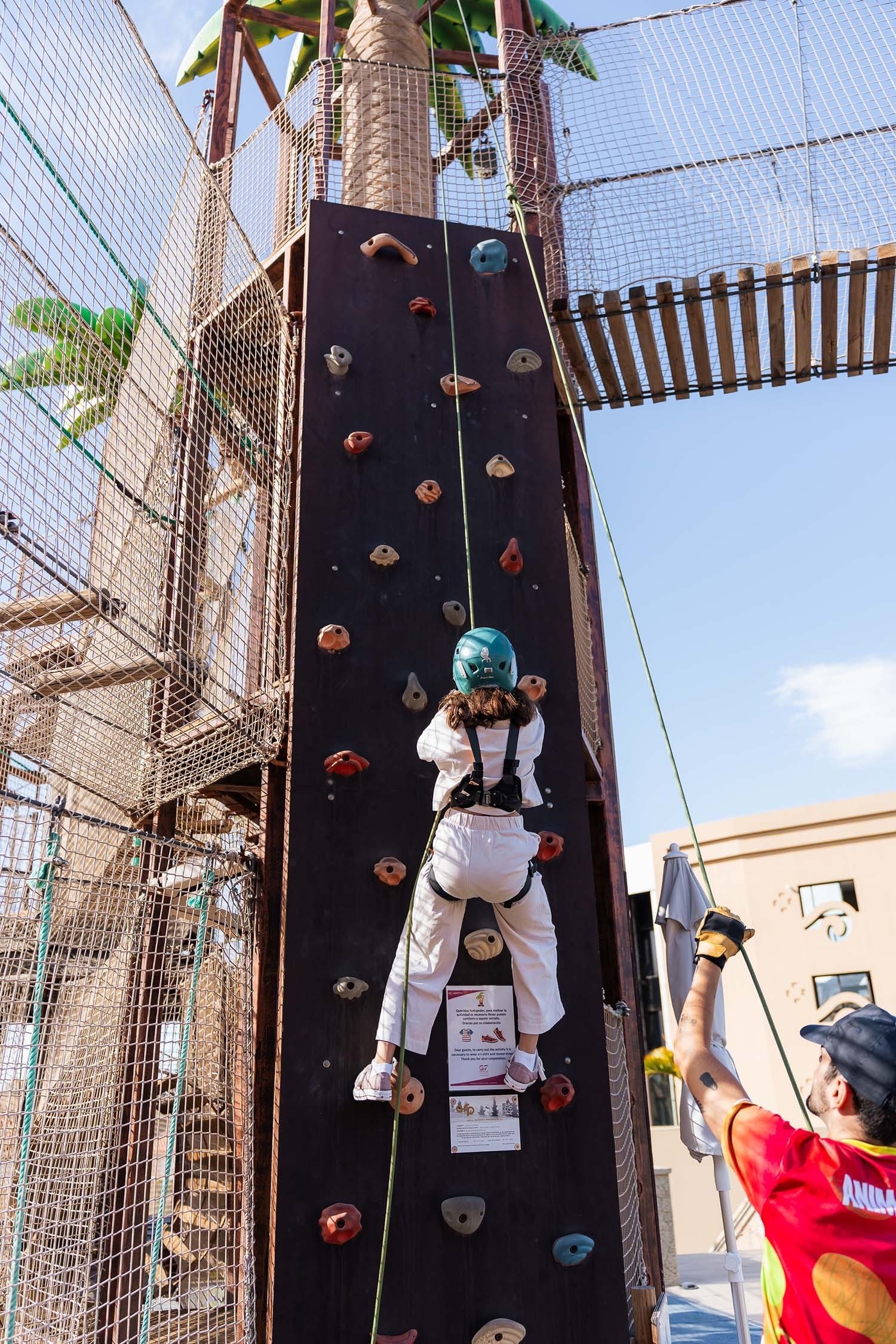 a child climbs a climbing wall while a man watches