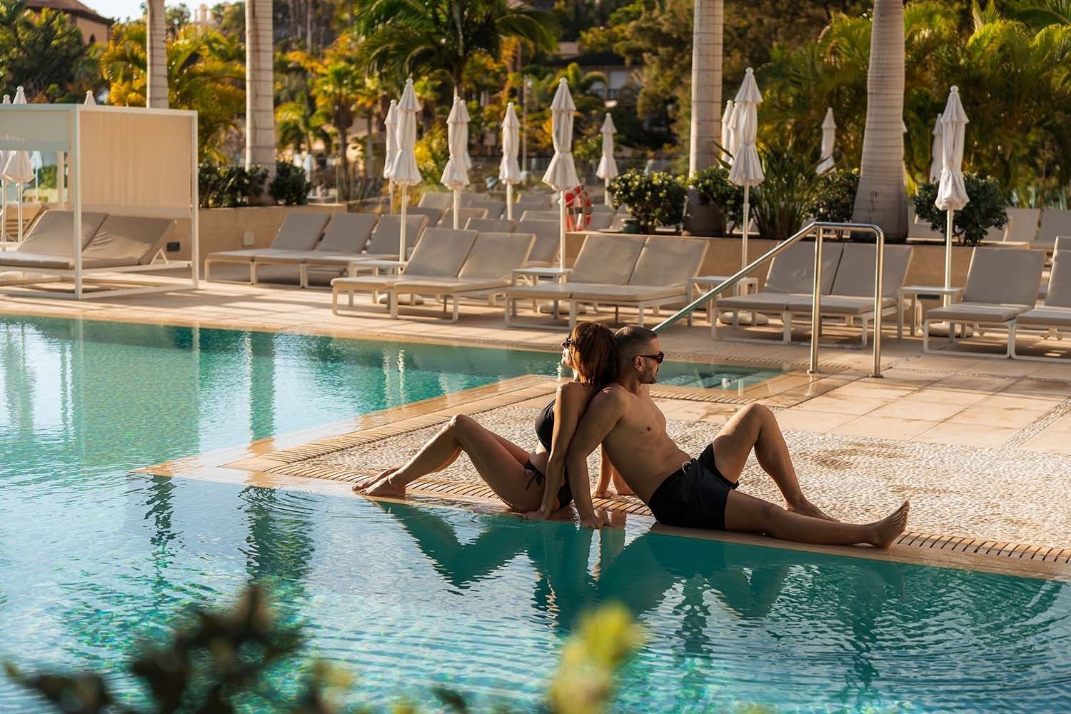 a man and a woman sit back to back in a swimming pool