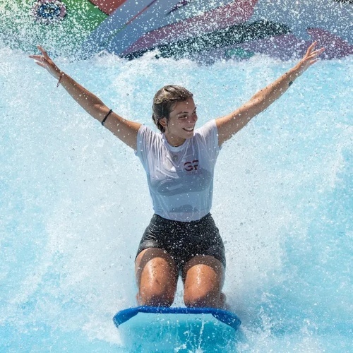 una mujer se sienta en una tabla de surf con los brazos abiertos