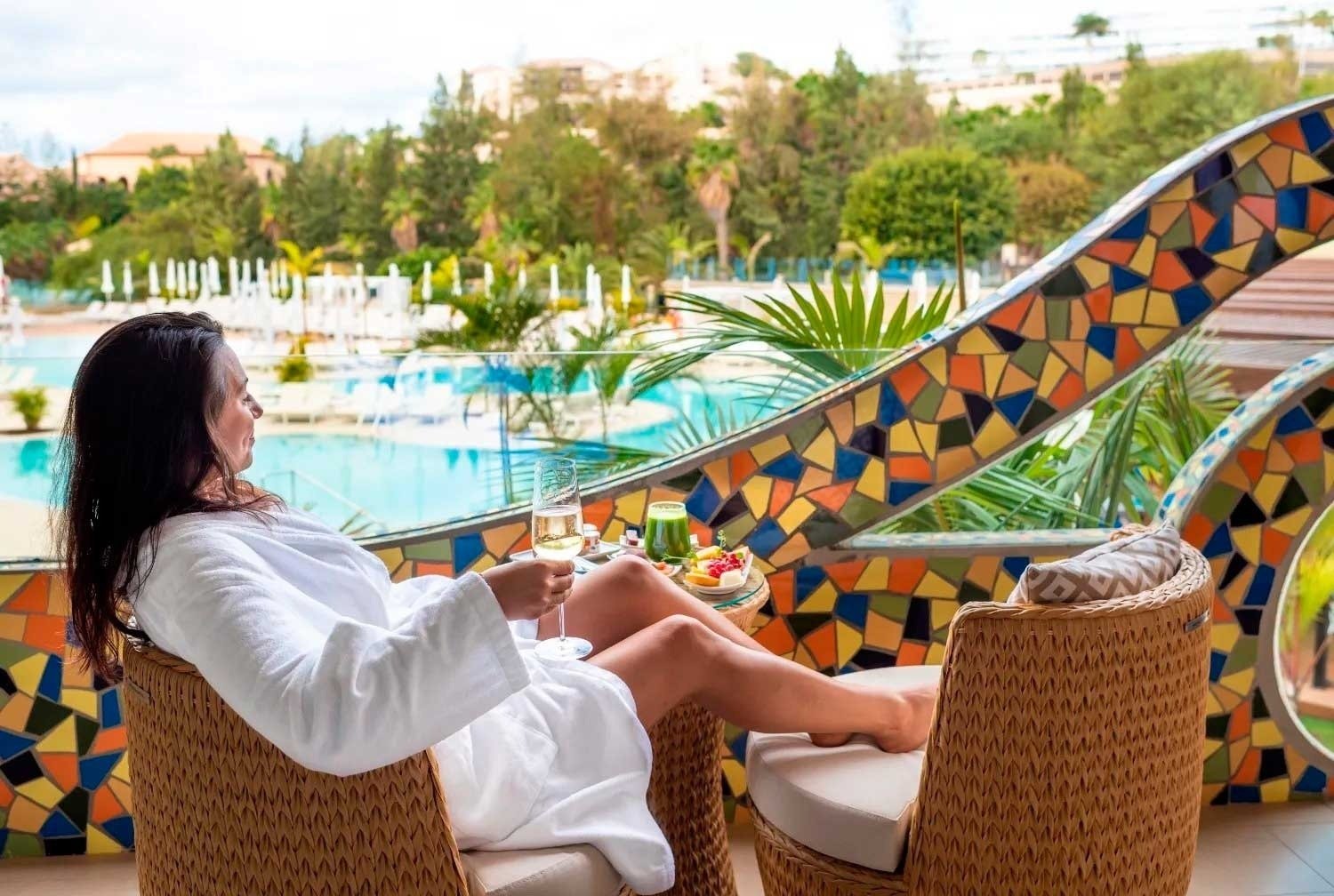 a woman in a bathrobe sits in a chair holding a glass of wine
