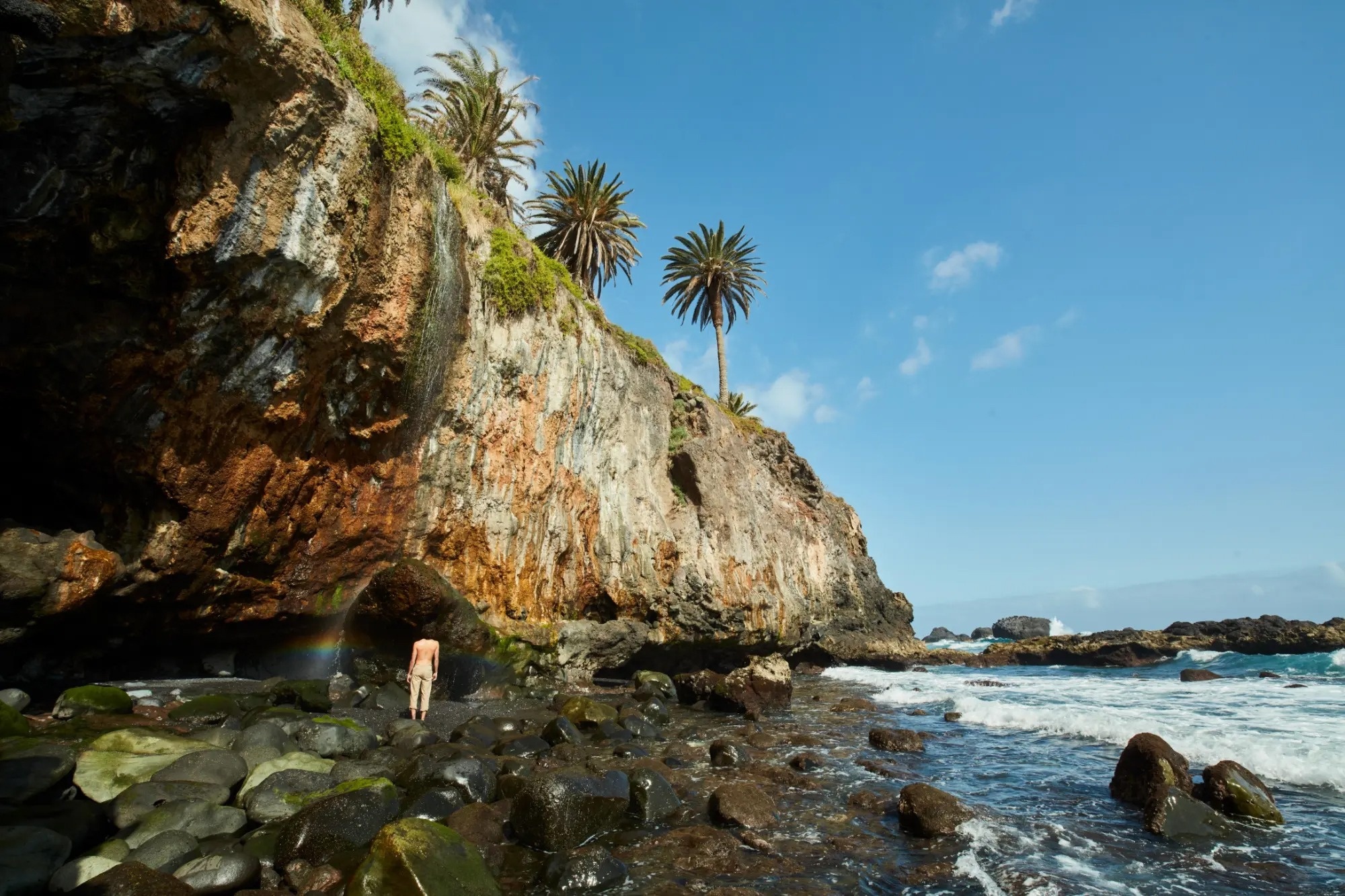 un hombre sin camisa está parado en una cueva junto al océano