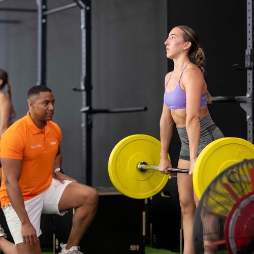 un hombre en una camisa naranja está mirando a una mujer levantando pesas