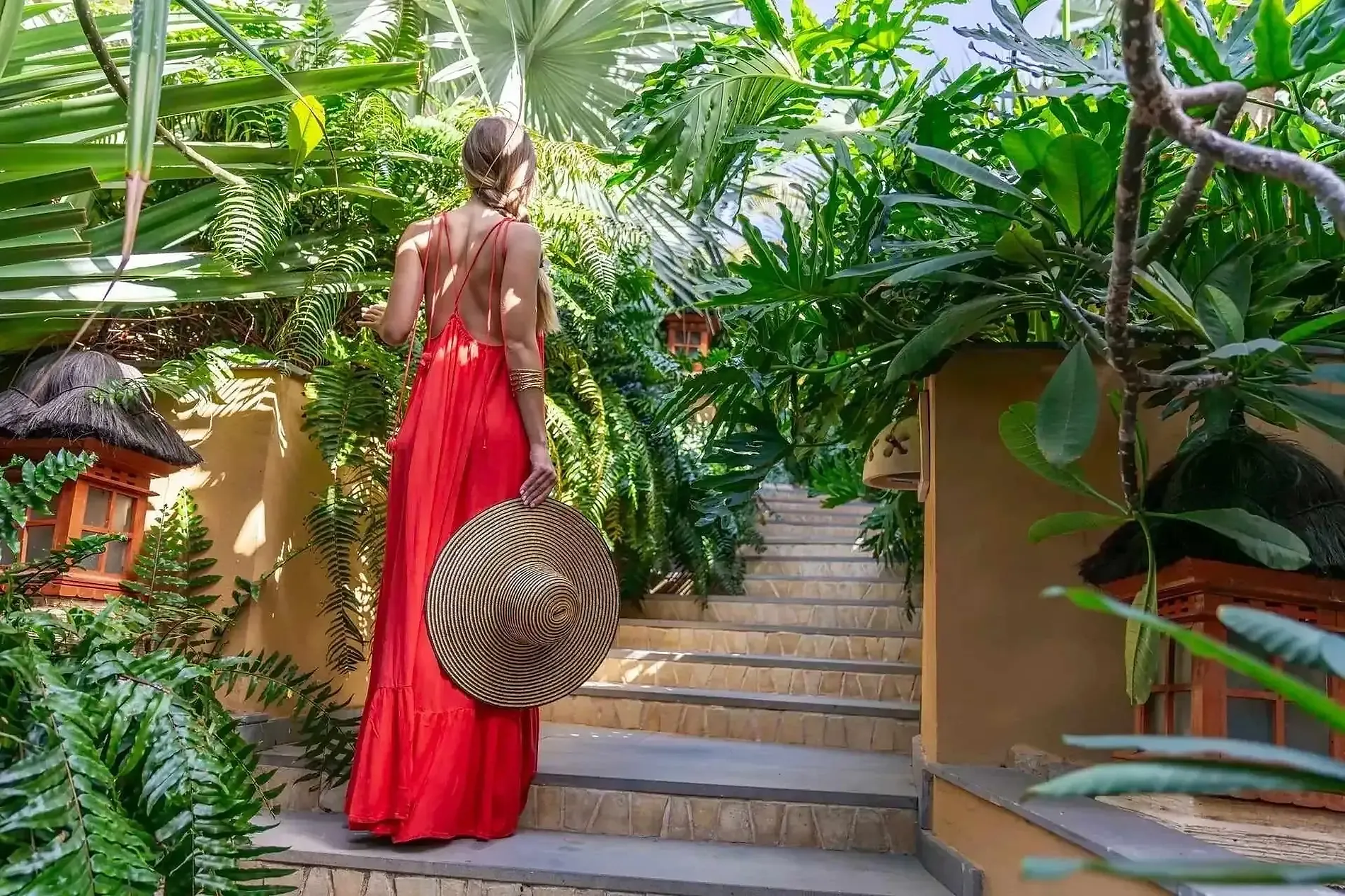 Woman in red dress holding hat on steps, Tenerife hotel exterior. Sustainability | Royal River Luxury Hotel