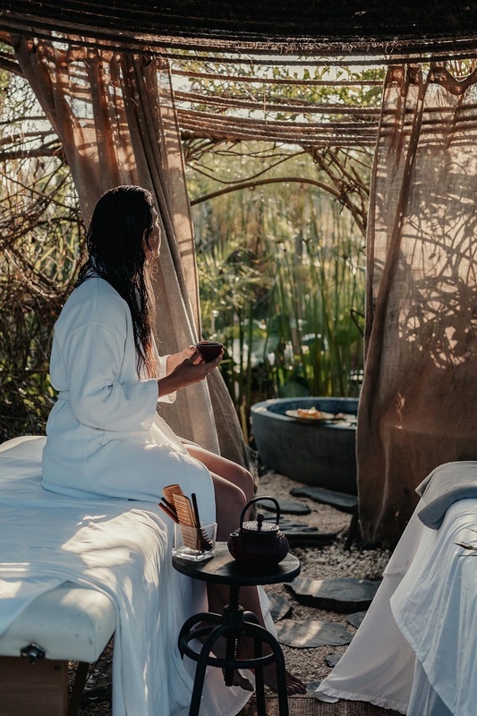 a woman in a bathrobe sits on a massage table holding a cup of tea