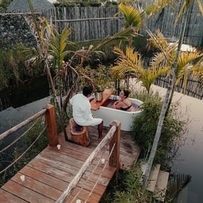 a man sits on a wooden dock next to a woman in a bathtub