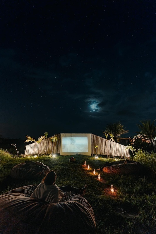 a woman sits on a bean bag in front of a large screen at night