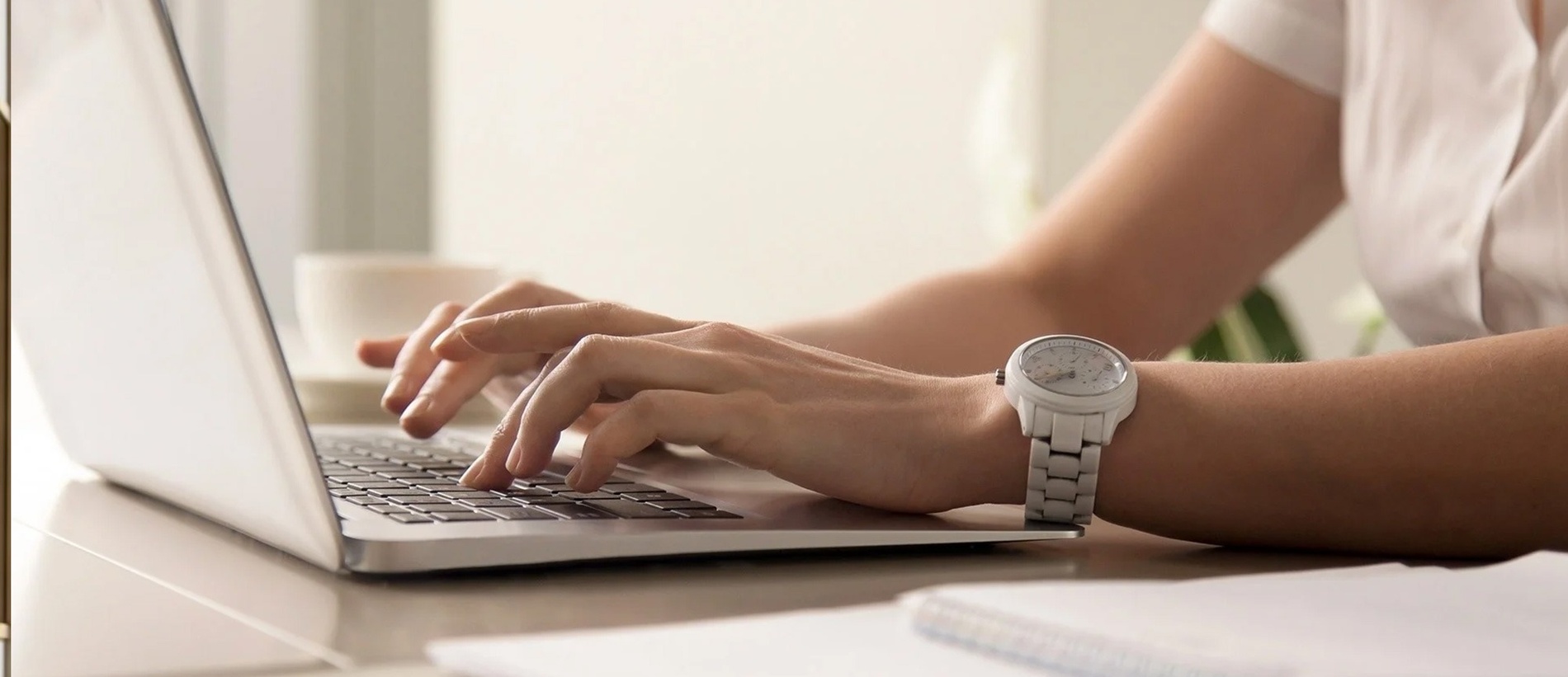 una mujer con un reloj en la muñeca está escribiendo en una computadora portátil