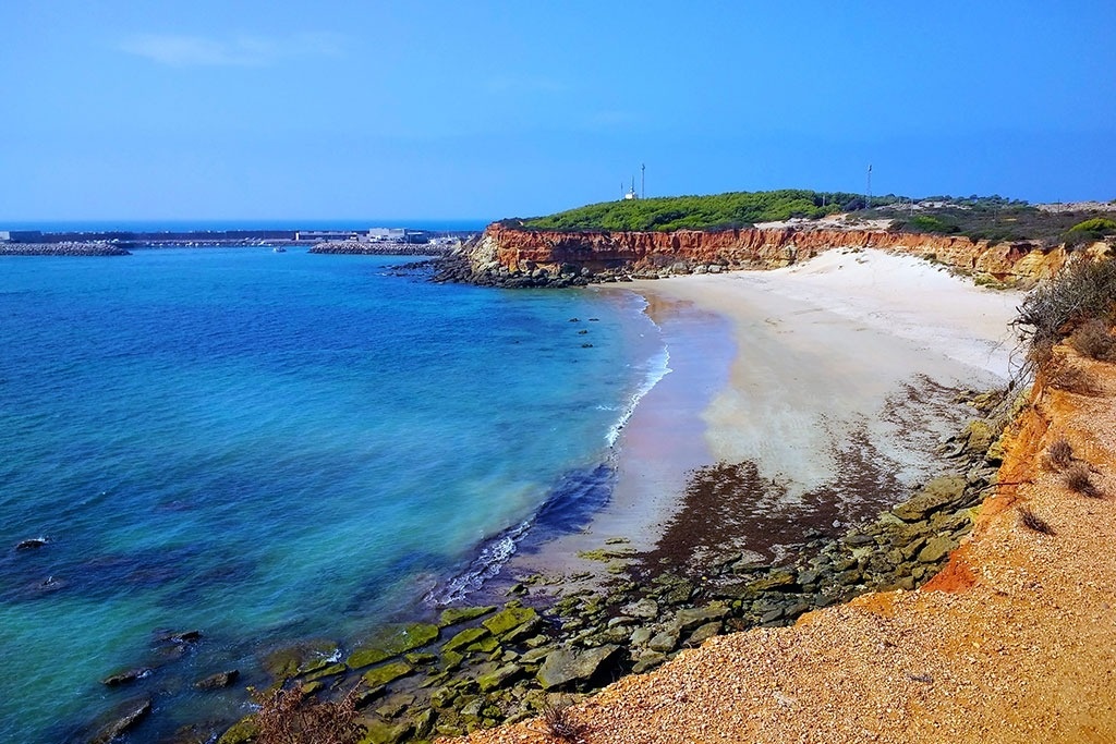 una playa con un acantilado rojo en el fondo