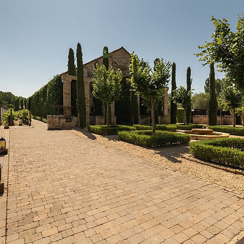 Paseo de ladrillo en Hacienda Zorita Wine Hotel con jardín, fuente y fachada rústica.