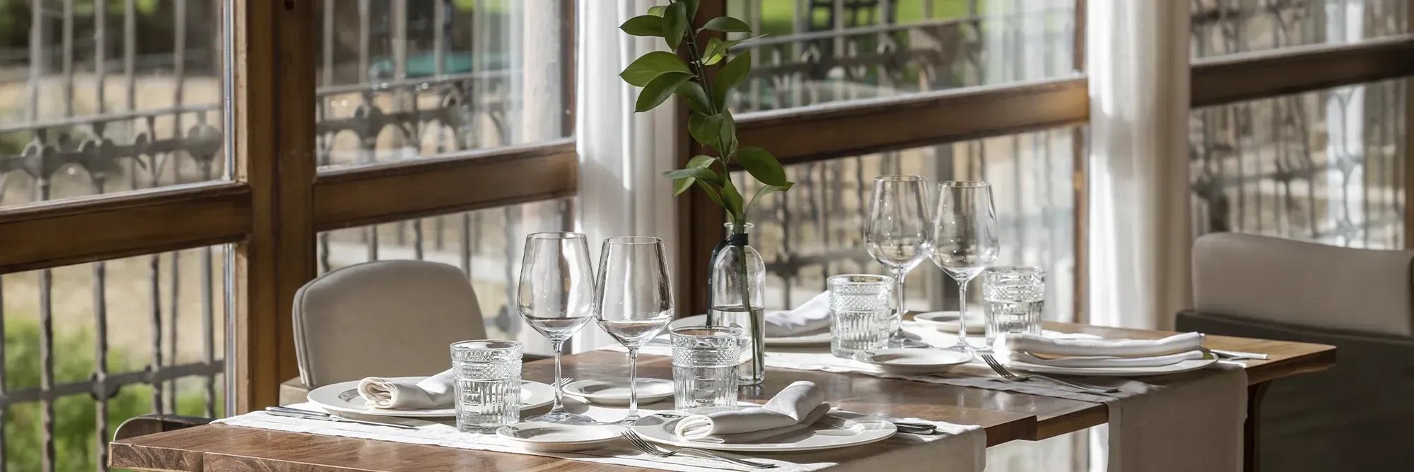 Mesa elegantemente puesta con vajilla, copas y flores en un restaurante con vista Hacienda Zorita Wine Hotel.