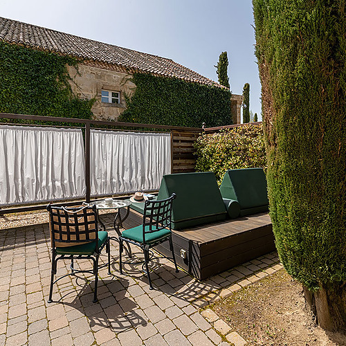 Terraza con tumbonas y mesa, junto a edificio cubierto de hiedra. Hacienda Zorita Wine Hotel ideal para relax.