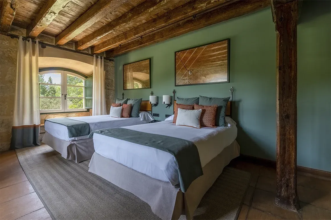 Habitación con dos camas gemelas, paredes verdes y vigas de madera. Hacienda Zorita Wine Hotel.