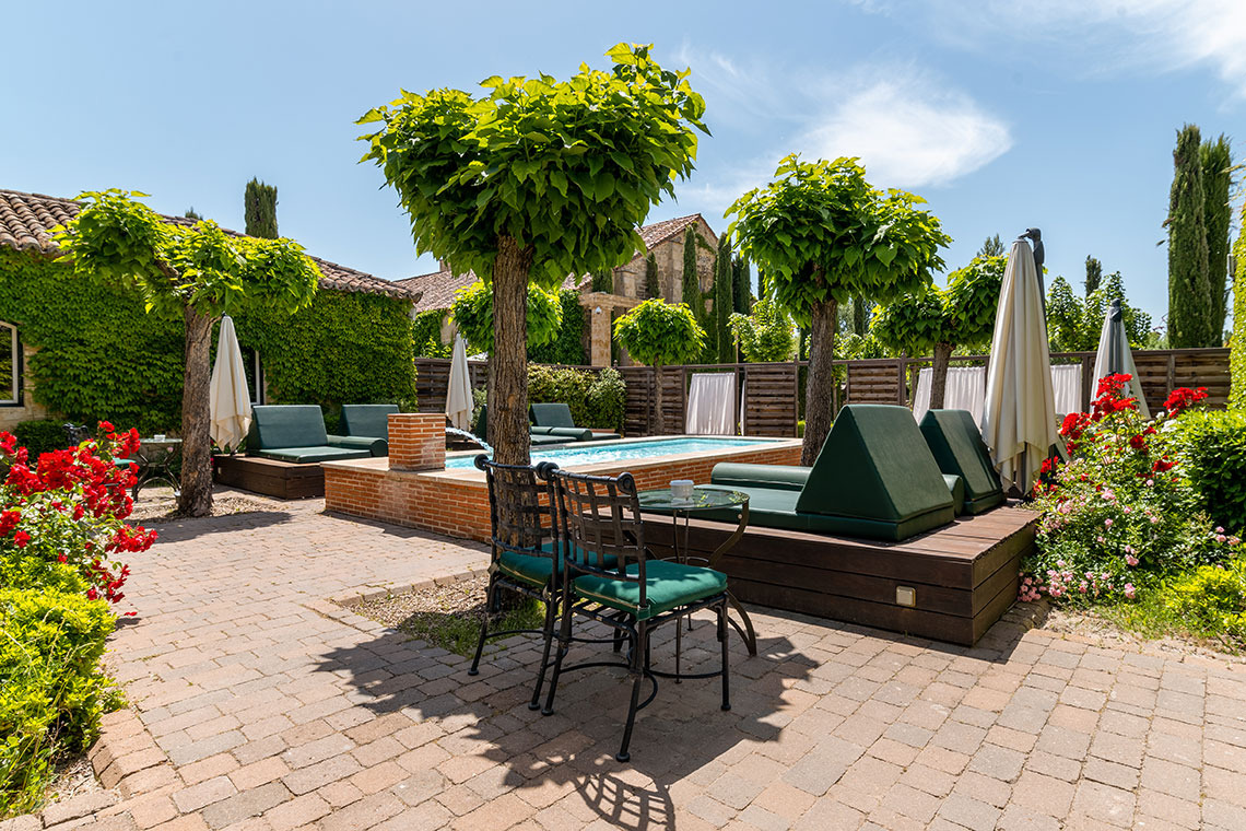 Hacienda Zorita Wine Hotel: piscina y tumbonas verdes, rodeada de flores rojas y árboles en un día soleado.