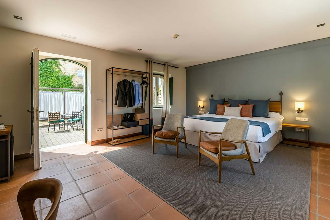 Habitación de hotel con cama, sillas y acceso a patio. Hacienda Zorita Wine Hotel.