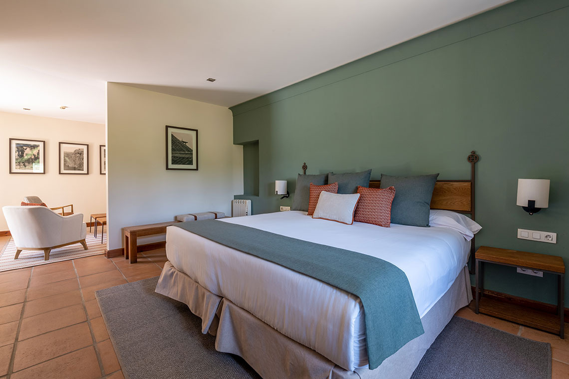 Habitación de hotel con cama grande, decoración verde yHacienda Zorita Wine Hotel, sala de estar adyacente.
