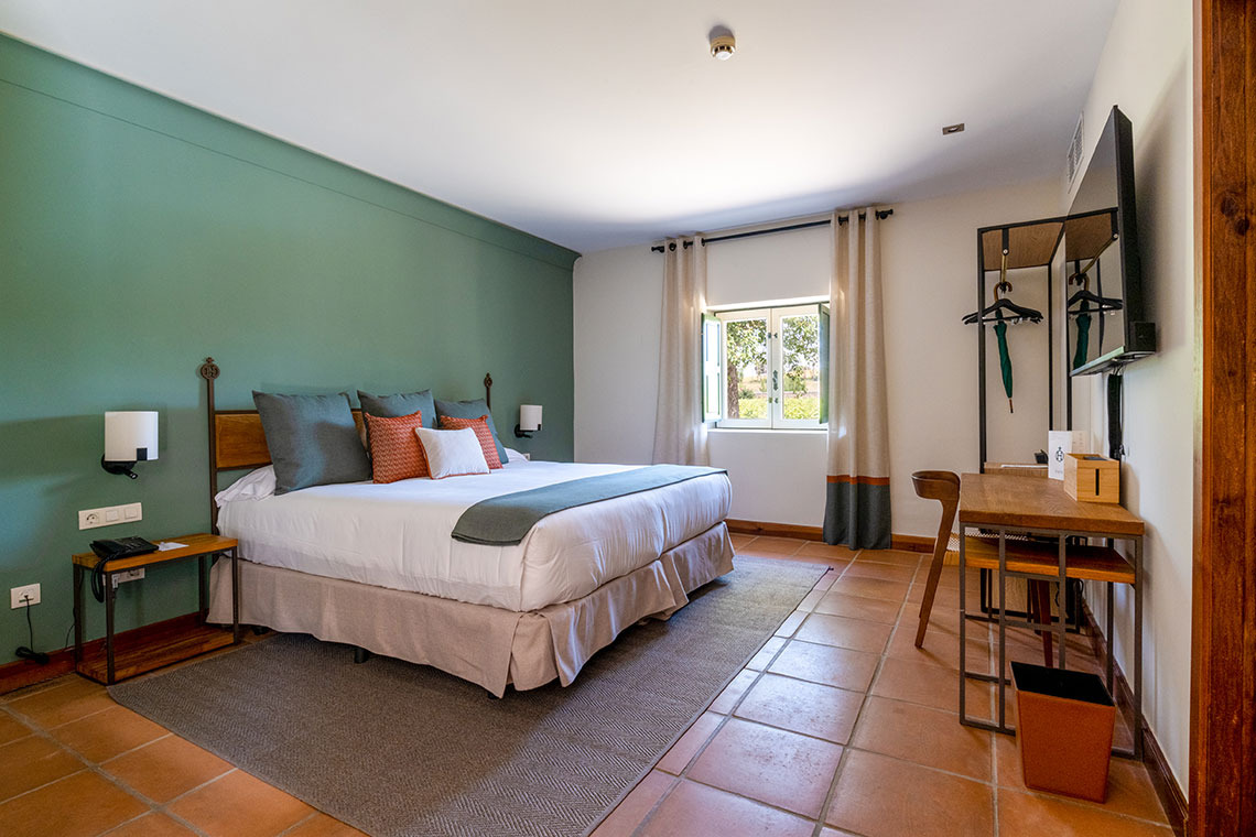 Habitación de hotel con cama king, verde y escritorio de madera. Hacienda Zorita Wine Hotel
