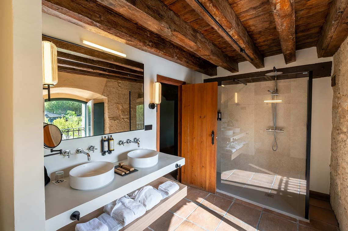 Baño de lujo con doble lavabo, ducha acristalada y vigas de madera. Hacienda Zorita Wine Hotel