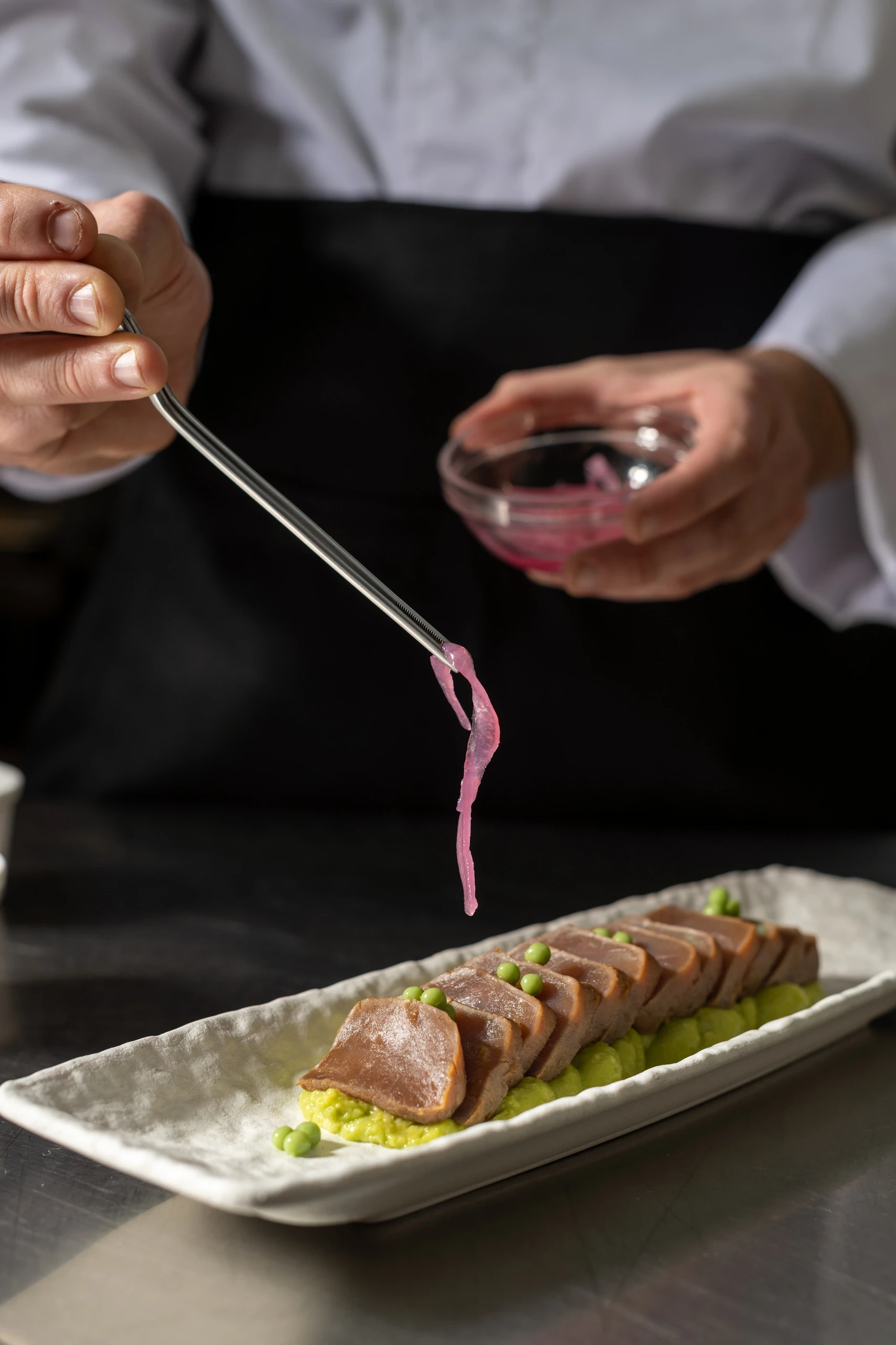 Chef garnishes sliced tuna with pink pickled onions using tweezers, completing a Hacienda Zorita Wine Hotel dish.