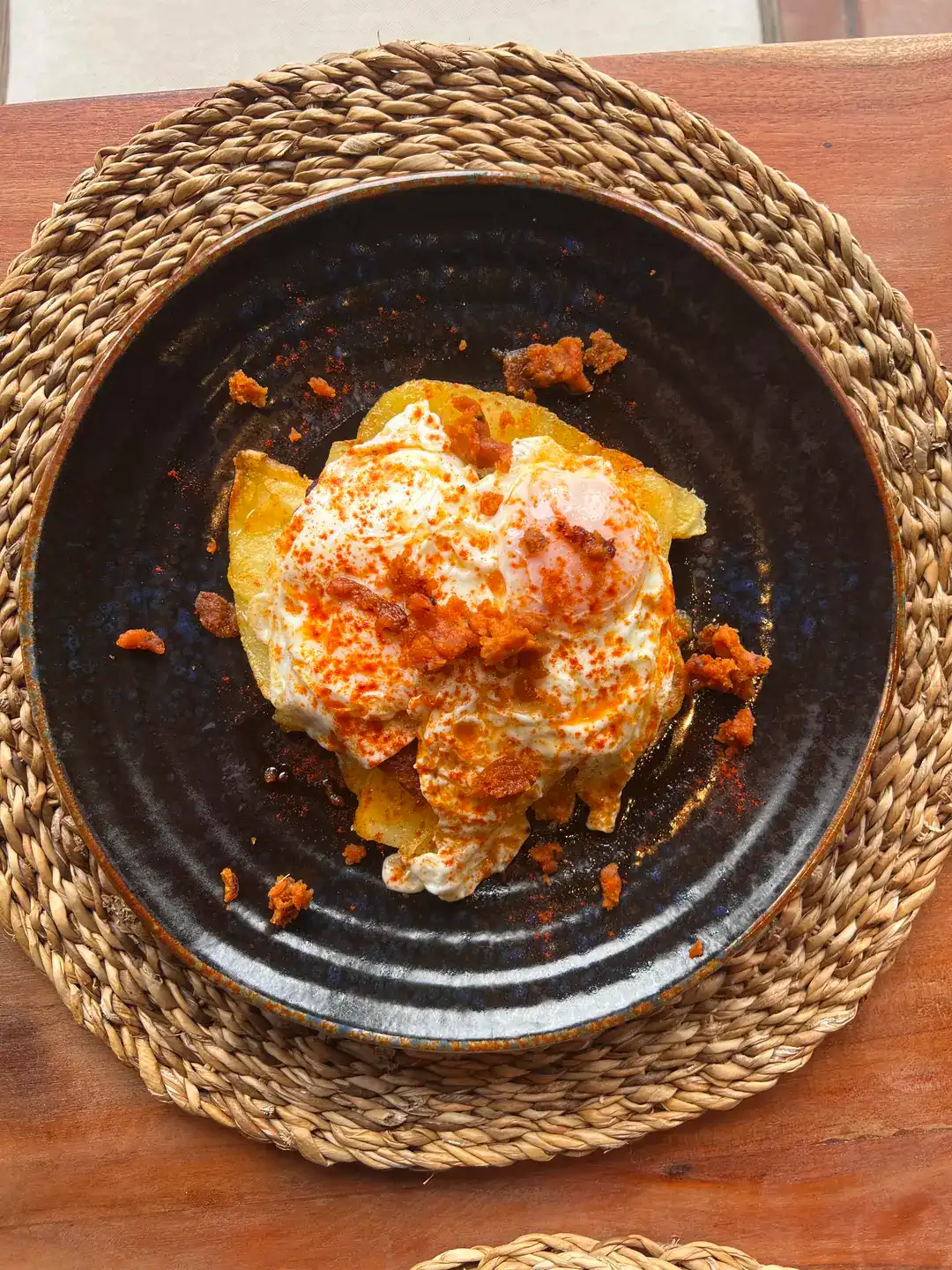 Deconstructed eggs with potatoes, paprika, and chorizo, served on a rustic plate on a woven placemat. Hacienda Zorita Wine Hotel