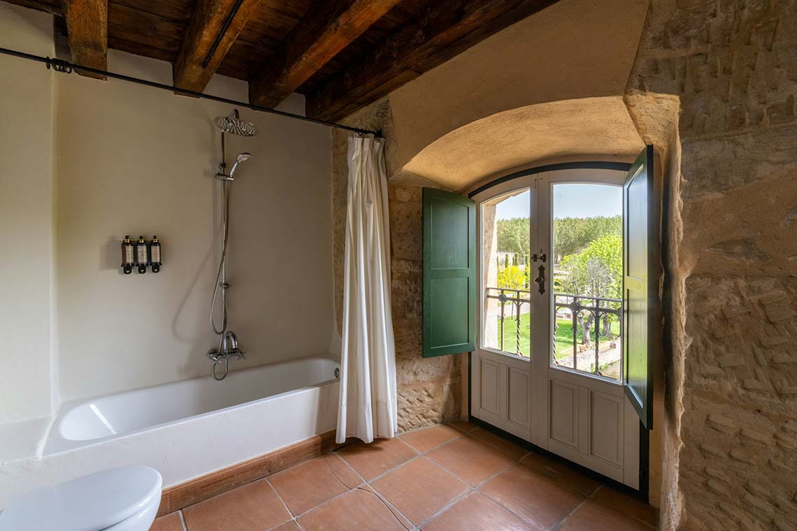 Baño rústico con bañera, ducha y balcón con vistas al campo, ideal para tu estancia Hacienda Zorita Wine Hotel.
