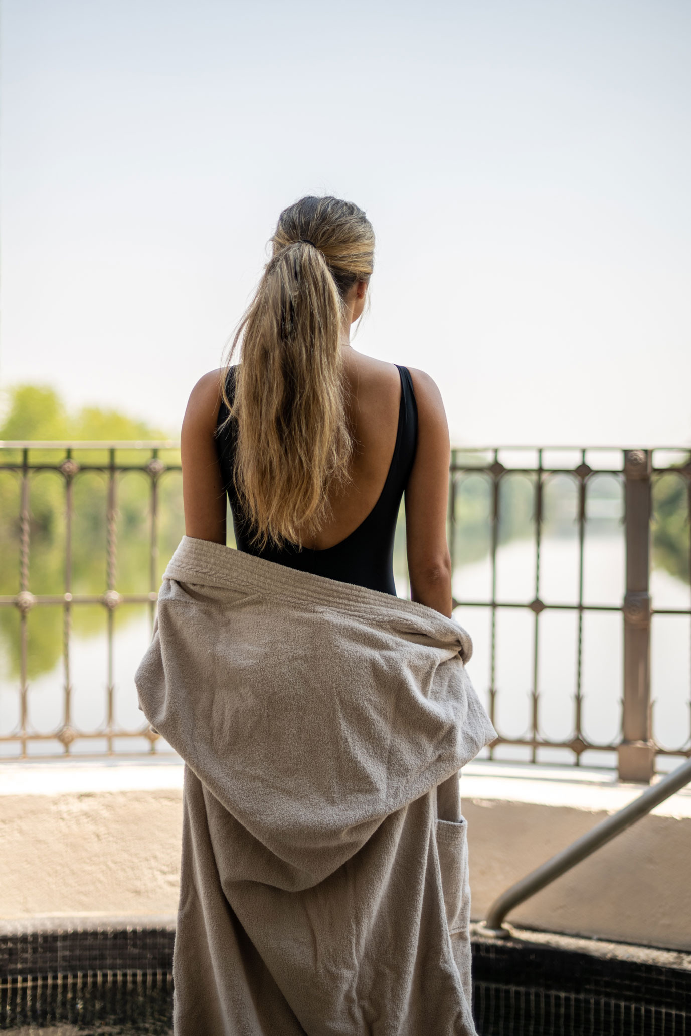 Woman in swimsuit and robe by pool, with water and greenery in background, a Hacienda Zorita Wine Hotel view.