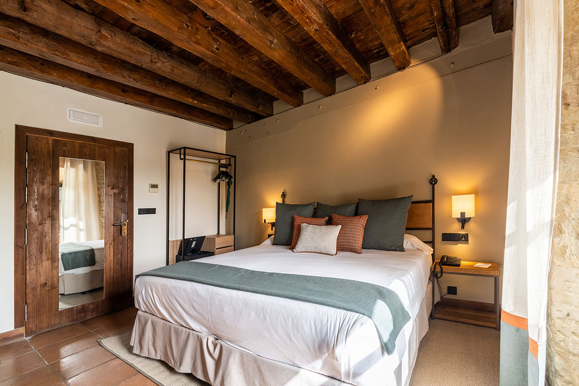 Habitación rústica con cama queen y vigas de madera, ideal para tu Hacienda Zorita Wine Hotel.