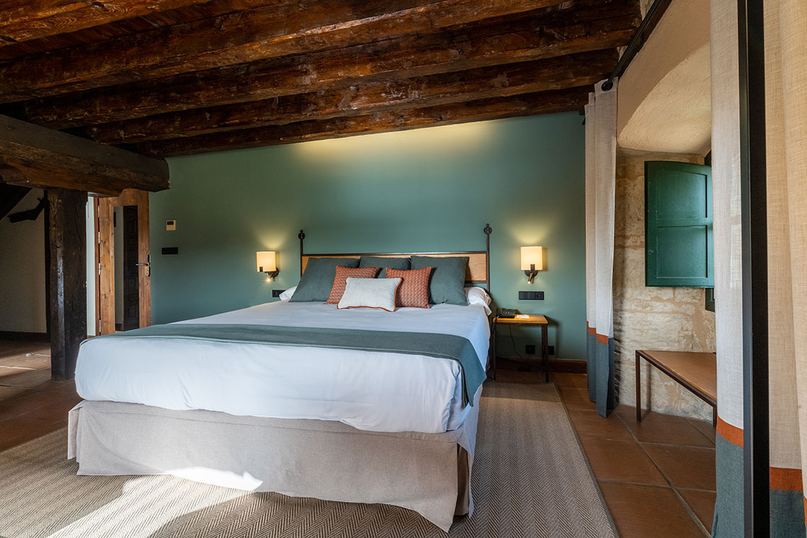 Cama matrimonial en habitación de hotel rústico con techos de madera y Hacienda Zorita Wine Hotel verde.