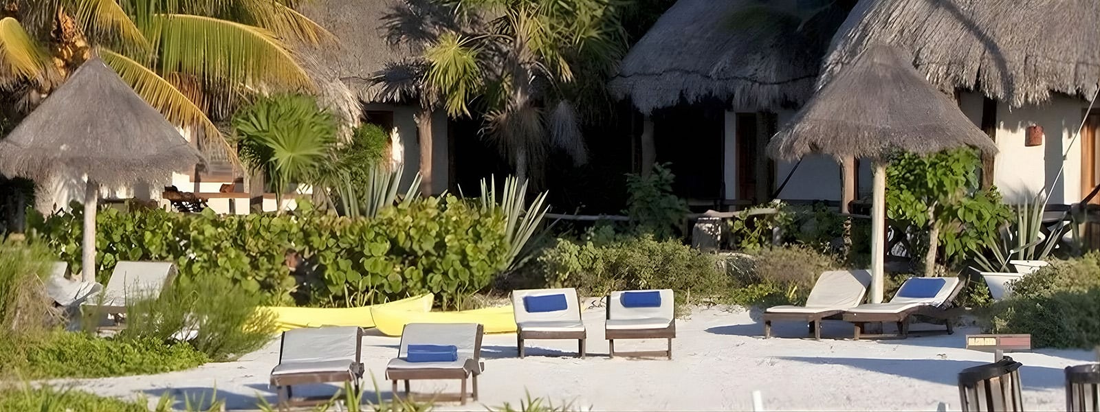 Holbox by Xaloc: cabañas tropicales con techo de paja en la playa con tumbonas y palmeras.