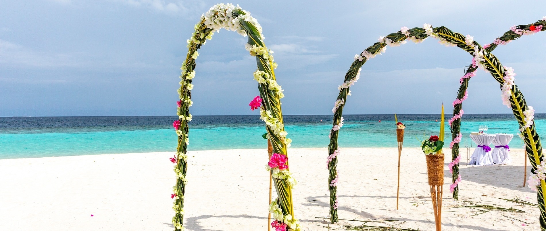 Un escenario idílico de boda en la playa con arcos florales, arena blanca y mar turquesa bajo un cielo despejado.
