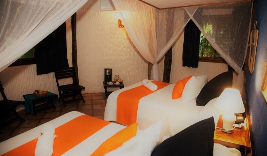 Un acogedor dormitorio con dos camas vestidas con mosquiteros, detalles naranjas y negros, y un ambiente rústico.