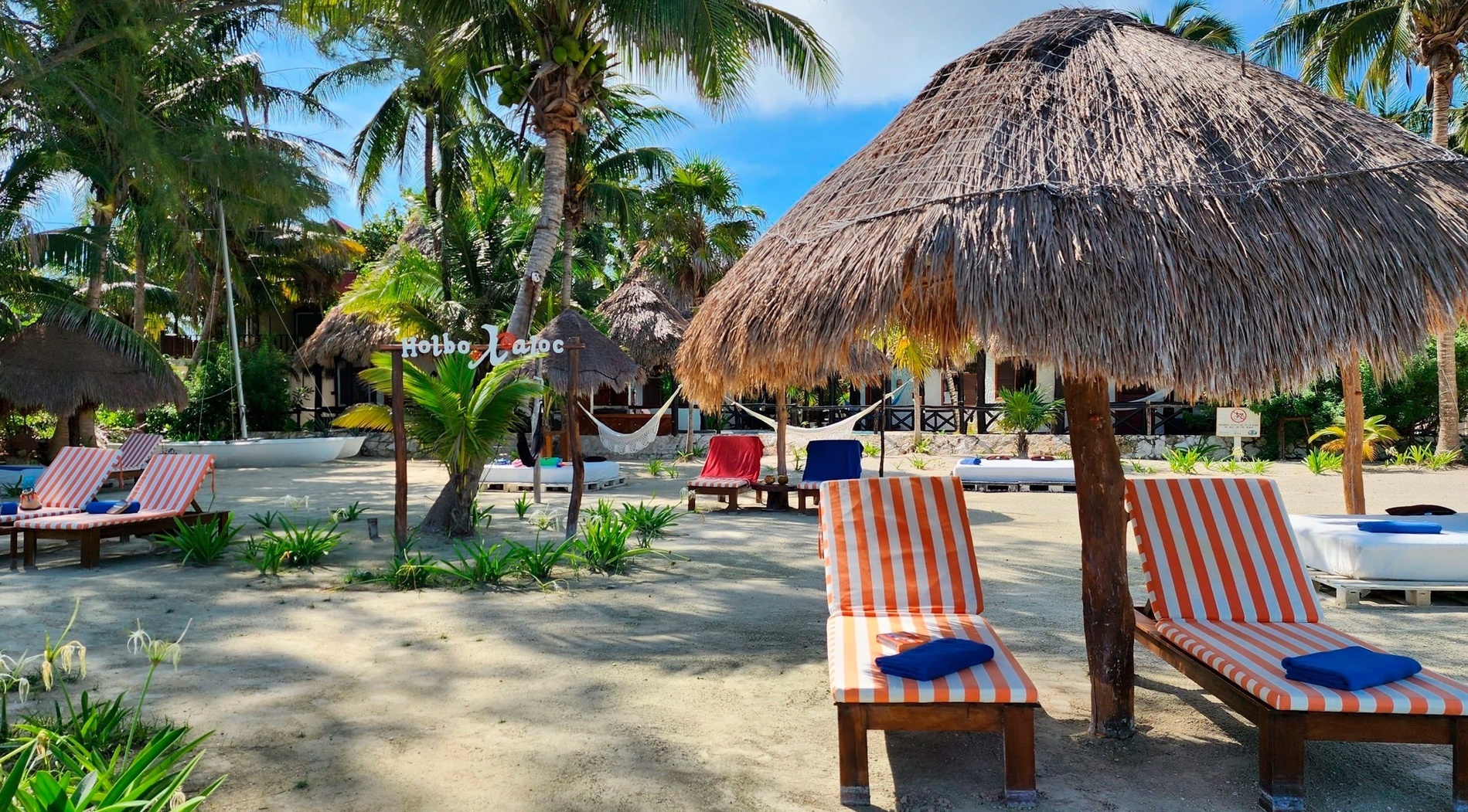Una idílica playa tropical en Holbox Xaloc con palmeras, tumbonas a rayas y palapas bajo un cielo azul brillante.