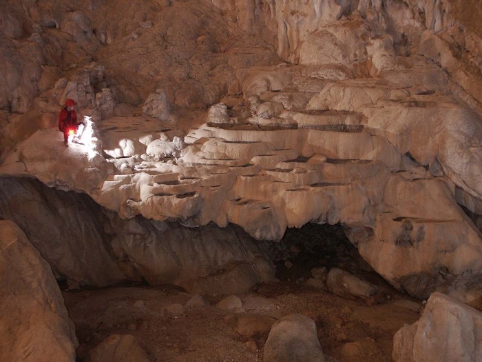 Persona explorando cueva con luz, mostrando formaciones rocosas.
