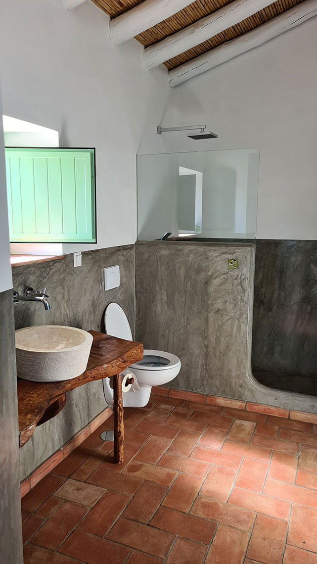 Banheiro rústico com pia de pedra, vaso sanitário e chuveiro. Horta de Bufenha hotel.
