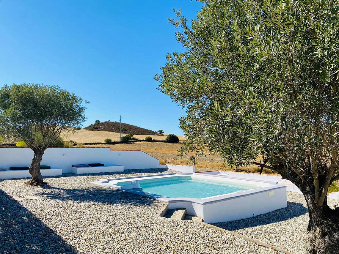 Piscina convidativa num pátio de cascalho com assentos brancos e árvore Horta de Bufenha.