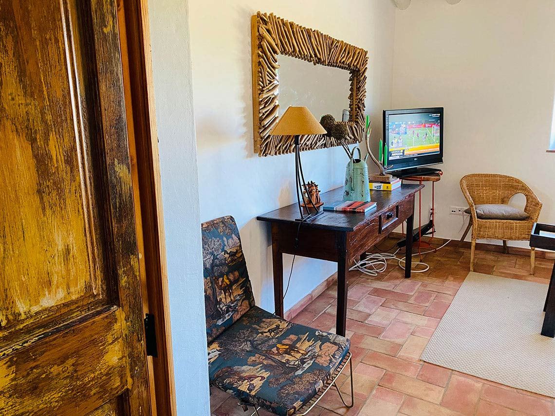Horta de Bufenha: Espaço aconchegante com TV, espelho rústico e cadeiras decoradas.