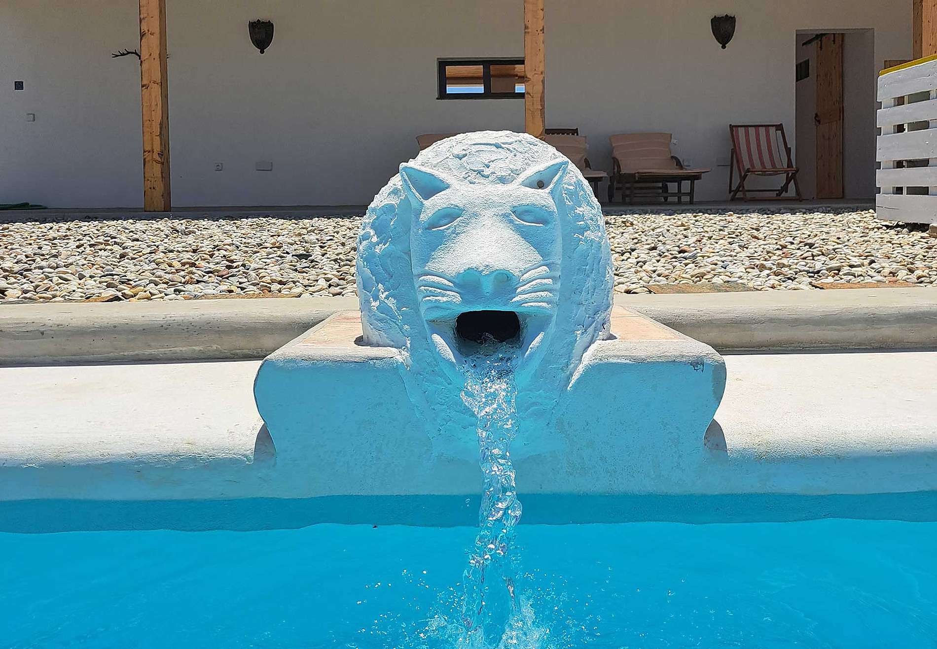 Horta de Bufenha: Fonte de leão branca em piscina azul, com área externa de pedras e móveis.
