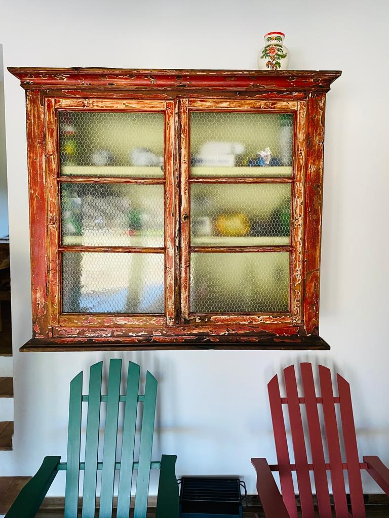 Armário antigo em madeira vermelha em um hotel Horta de Bufenha com cadeiras coloridas ao fundo.