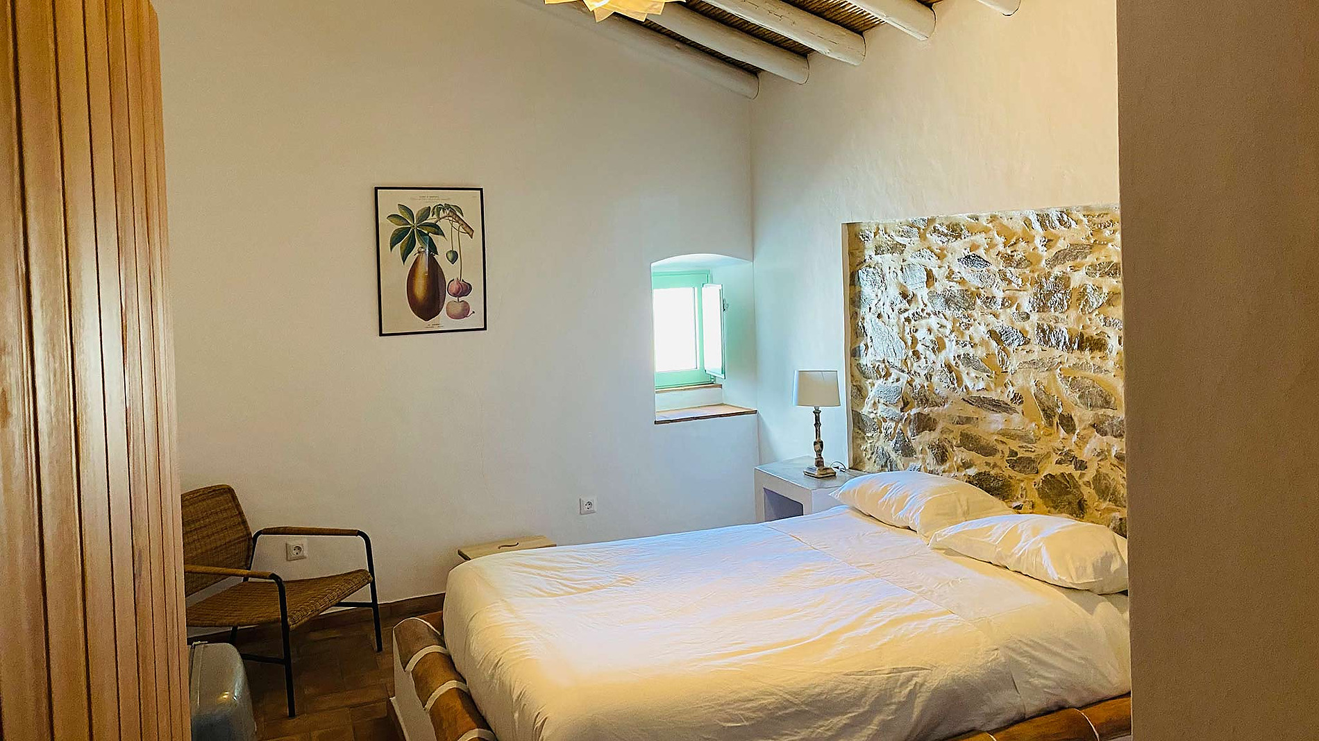 Quarto aconchegante com cama de casal, cabeceira de pedra, janela charmosa e um quadro decorativo Horta de Bufenha.
