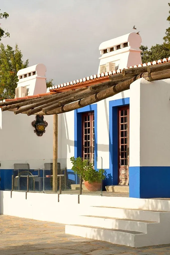 Fachada branca com detalhes em azul, janelas de madeira e varanda. Horta da Moura