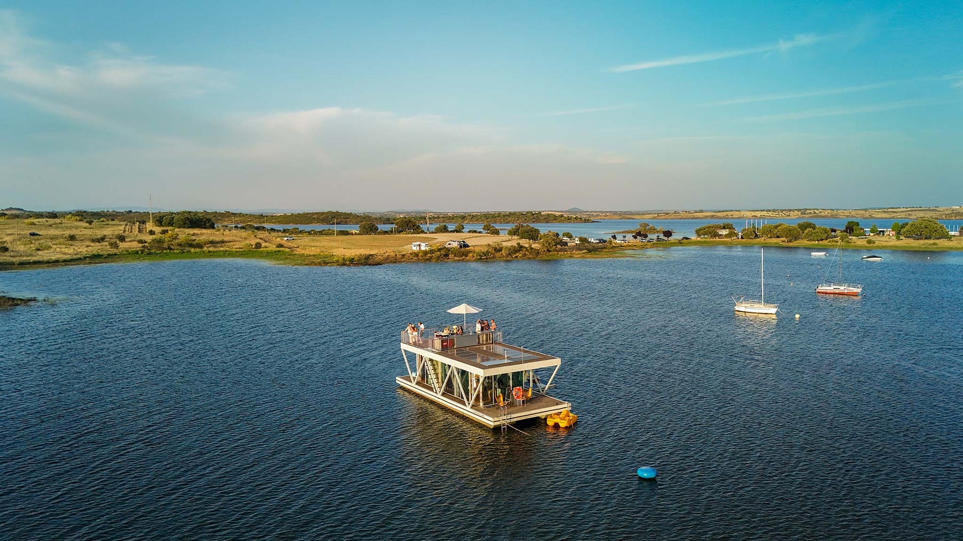 Casa flutuante de luxo Horta da Moura em lago sereno com barcos e paisagem natural
