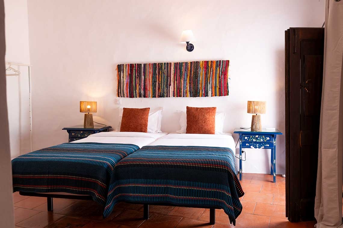 Habitación con dos camas individuales en Horta da Moura, decorada con mantas azules y cojines naranjas.
