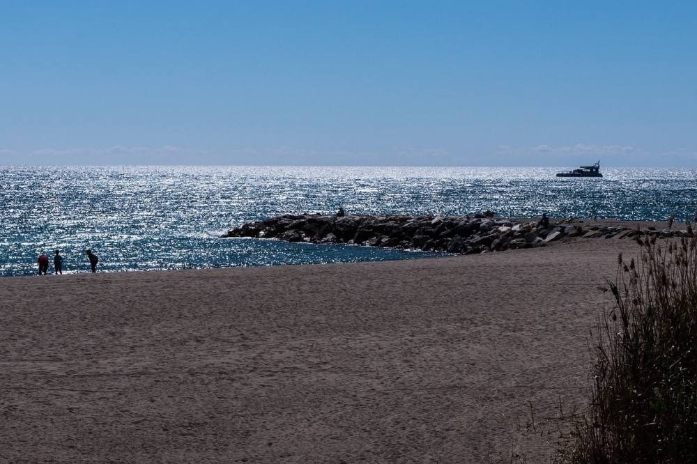 dos personas caminan por la playa con un barco en el horizonte