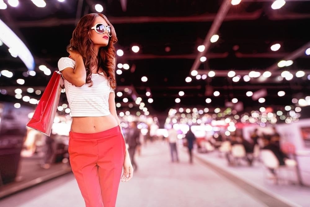 una mujer con gafas de sol y pantalones rojos sostiene una bolsa de compras roja
