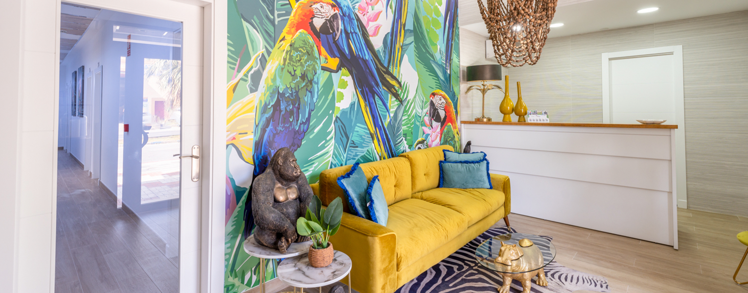 una sala de estar con un sofá amarillo y un mural de loros en la pared