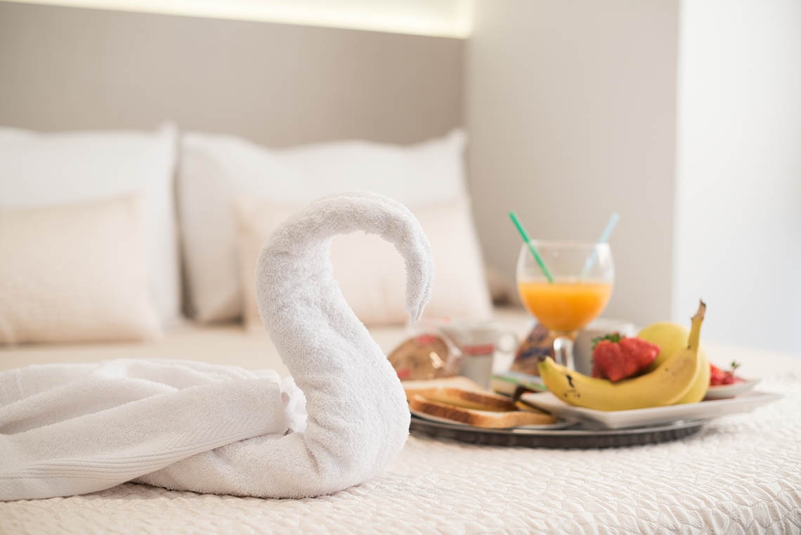 una cama con una toalla en forma de cisne y una bandeja de desayuno